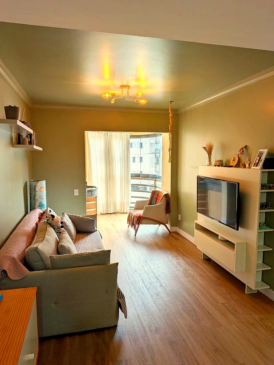 Sala de estar ampla, com sofá, painel de TV e porta para a varanda